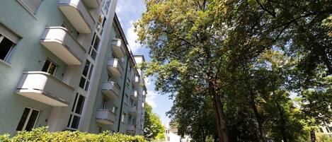 Un immeuble résidentiel à plusieurs étages, doté de balcons et entouré d’une végétation luxuriante et d’arbres.