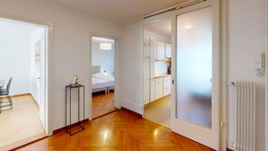 A modern apartment with a wooden floor, a bed, a small table with a decorative item, and white cabinets.