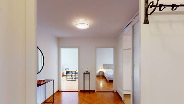 A modern apartment with a wooden floor, a dining area with a table and chairs, and a bedroom with a bed and nightstand.