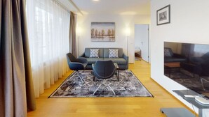 Ein modernes Wohnzimmer mit einer Couch, zwei Sesseln, einem Fernseher und einem Gemälde an der Wand.