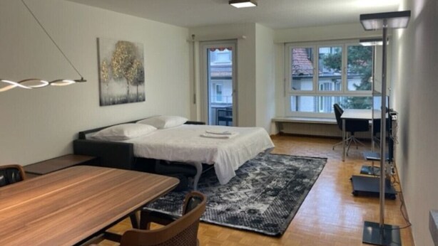 A modern bedroom with a bed, bedside table, and a desk area. - Cozy, sunny, city center 1BR flat (Marble 3) (Zürich)