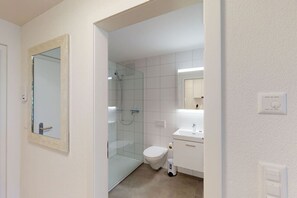Ein modernes Badezimmer mit Duschabtrennung aus Glas, Toilette und Waschbecken mit Spiegel darüber.