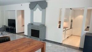 A modern living room with a fireplace, a dining table, and a kitchen area visible through an open door.