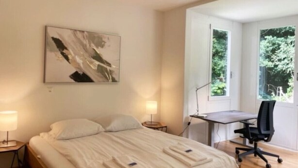 A hotel room with a bed, bedside tables, a desk, and a chair.