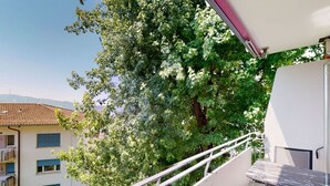 Een balkon met een tafel en stoelen, met uitzicht op een boom en een gebouw met pannendak.