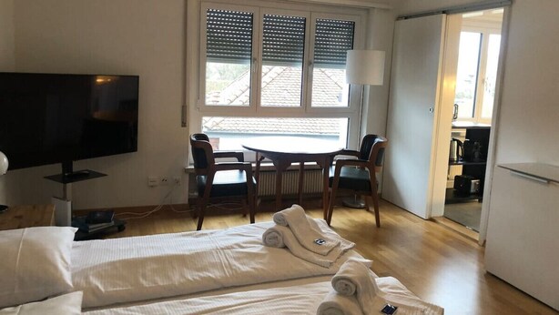 Ein Hotelzimmer mit Bett, Fernseher, Esstisch mit Stühlen, einem Fenster mit Jalousien und einer Tür zu einer Küche.