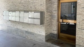 Ein Gebäudeeingang mit steinverkleideter Fassade, einer Glastür und einer Reihe von Briefkästen an der Wand.