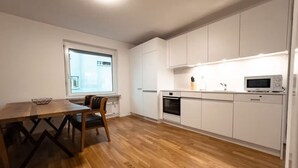 A modern kitchen with white cabinets, a wooden dining table, and a built-in oven. - Fantastic 2BR in the city center (Sky7) (Zürich)