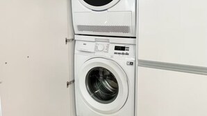 A stacked washer and dryer unit in a corner of a room with a wooden floor. - Fantastic 2BR in the city center (Sky7) (Zürich)