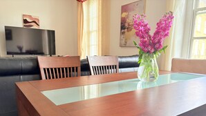 A dining area with a wooden table, chairs, a sofa, and a TV in the background.