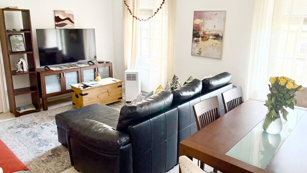A living room with a sofa, a TV, a wooden cabinet, a small table, and a vase with flowers.