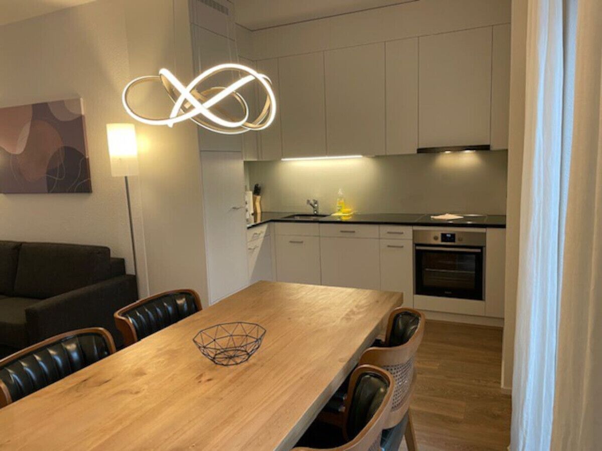 A modern kitchen with white cabinets, a wooden dining table, and a built-in oven.