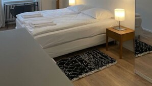 Ett sovrum med en säng, sänglampor, ett element, ett fönster och ett konstverk som hänger på väggen.