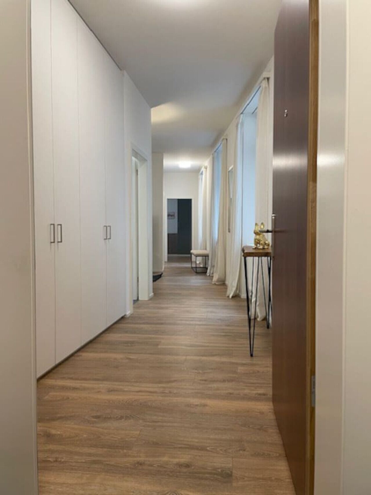 A narrow hallway with wooden flooring, white walls, and a door at the end.