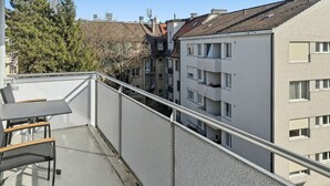 A balcony with a table and chairs, overlooking a residential area with multi-story buildings.