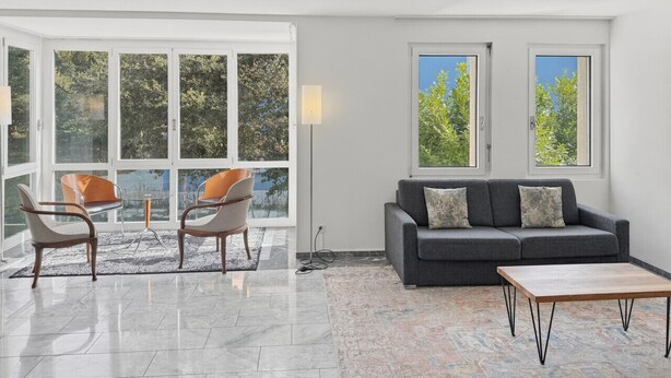 A modern living room with a sofa, two armchairs, a coffee table, and large windows offering a view of trees. - Amazing 2BR flat: spacious and central (Duke2) (Zürich)