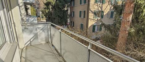 Un balcón con barandilla de metal que da a una zona residencial con edificios y árboles.