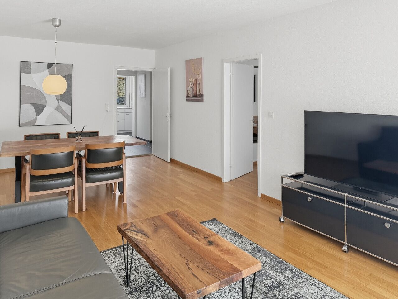 Ett modernt vardagsrum med ett matbord i trä, stolar, en soffa, en tv och en matta.