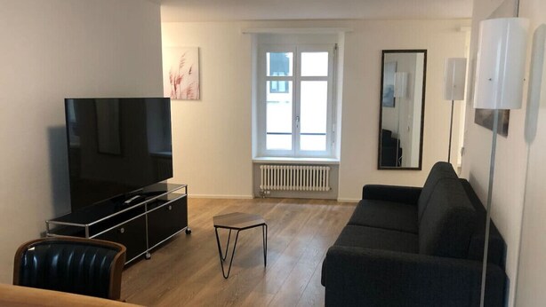 A modern living room with a flat-screen TV, a sofa, a coffee table, and a dining table. - Fantastic 2BR flat close to Paradeplatz (Canal2) (Zürich)