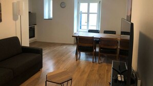 A living room with a sofa, a dining table with chairs, a TV, and a kitchen area with a stove. - Fantastic 2BR flat close to Paradeplatz (Canal2) (Zürich)