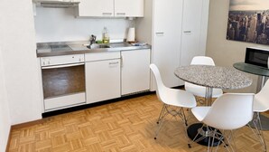 Une cuisine compacte avec des meubles blancs, un four encastré et un coin repas comprenant une table ronde et des chaises blanches.