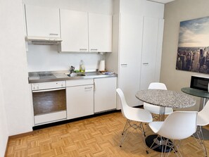 A compact kitchen with white cabinets, a built-in oven, and a dining area with a round table and white chairs.
