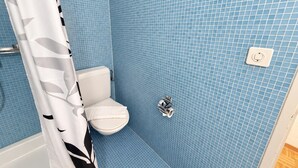 Une salle de bain avec des toilettes blanches, des murs recouverts de carreaux bleus et un rideau de douche à motifs noirs et blancs.