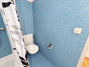 A bathroom with a white toilet, blue tiled walls, and a shower curtain with a black and white pattern.