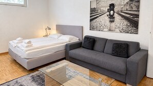 Une chambre moderne comprenant un lit, un canapé, une table basse en verre et un tableau représentant une voie ferrée, accroché au mur.