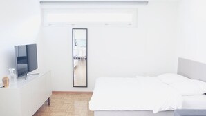 A modern bedroom with a bed, a TV on a white cabinet, and a mirror on the wall. - Charming studio in the city centre (Art 14) (Zürich)