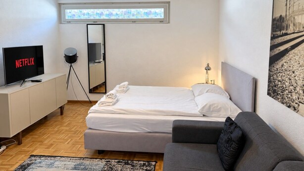 Une chambre d’hôtel moderne équipée d’un lit, d’un canapé, d’une télévision, d’un miroir et d’une fenêtre.