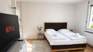 A modern bedroom with a large bed, a TV on a stand, and a small bedside table.