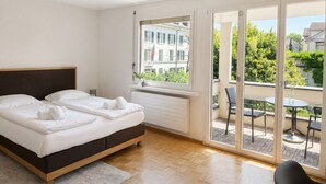 A hotel room with a bed, a window, and a balcony with chairs and a table.
