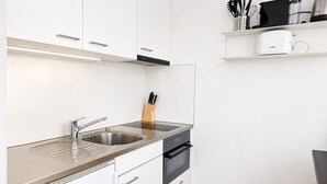 A compact kitchen with a stainless steel sink, a built-in oven, and white cabinetry. - Terrific studio in the city centre (Art 9) (Zürich)