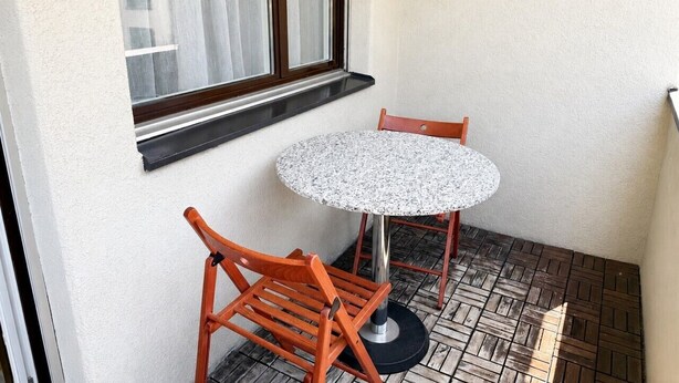 A small outdoor seating area with a round table and two wooden chairs, a window with blinds, and a tiled floor. - Terrific studio in the city centre (Art 9) (Zürich)