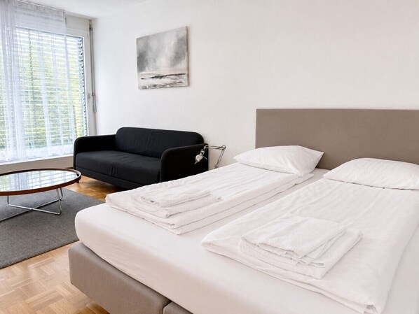 A hotel room with a bed, a round table, a black armchair, and a painting on the wall.