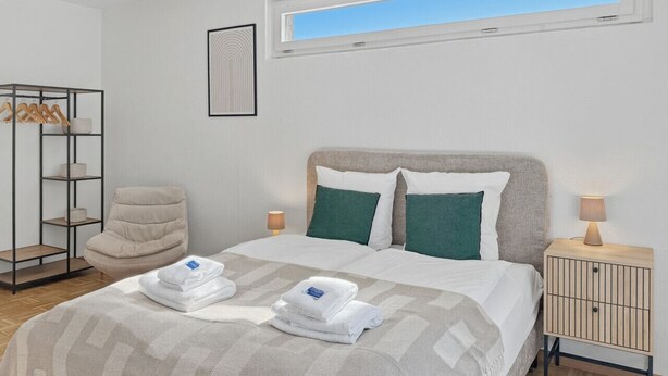 Een keurig opgemaakt slaapkamer met een bed, een stoel, een plank en een nachtkastje.