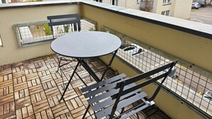 Een balkon met een ronde tafel en bankjes, een betegelde vloer, en gebouwen in de verte.