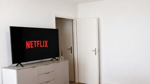 A room with a television on a stand displaying the Netflix logo, a door, and a white wall. - Cozy studio in the city centre (Art 13) (Zürich)