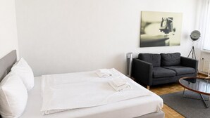 A modern bedroom with a bed, a sofa, a small table, and a floor lamp. - Cozy studio in the city centre (Art 13) (Zürich)