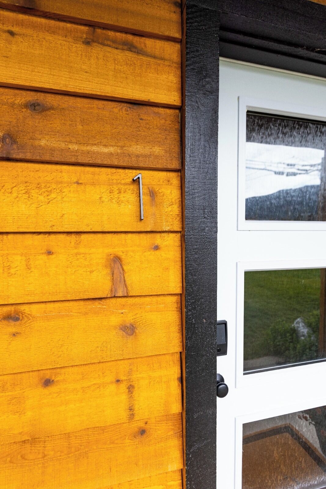 Een houten buitenmuur met een bord met het cijfer '1', een witte deur met ruitpanelen en een zwart deurkozijn.