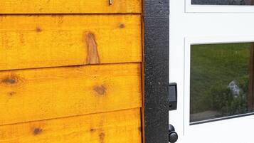 Een houten buitenmuur met een bord met het cijfer '1', een witte deur met ruitpanelen en een zwart deurkozijn.