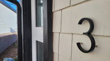 Husnummer ’3’ på en beige vägg, ett fönster och en del av en vit dörrkarm.