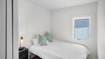 Un dormitorio con cama, dos almohadas, una mesita de noche con lámpara, una ventana con vistas y una puerta.