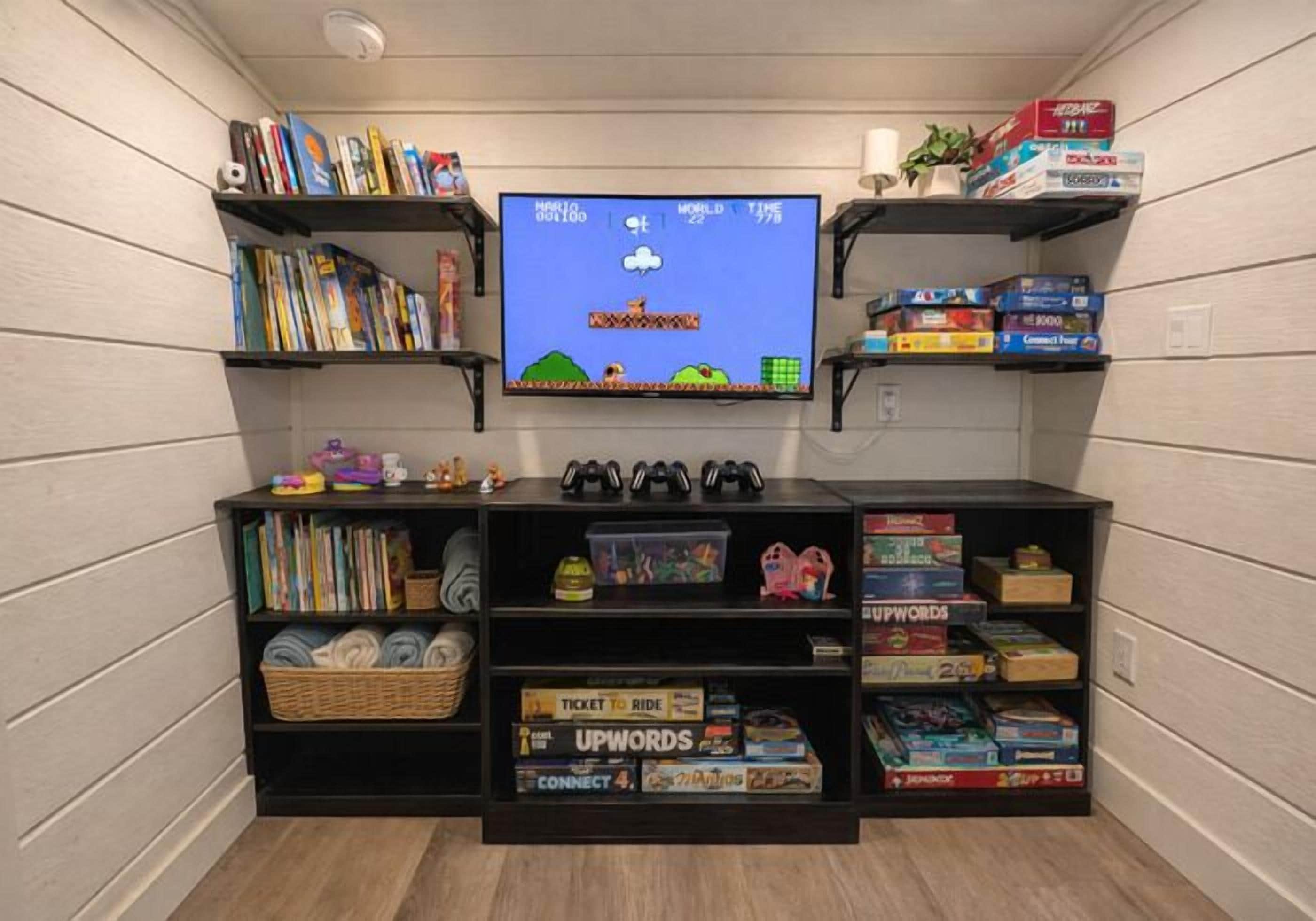 A room with a television displaying a game, shelves with books and games, and a basket of board games.