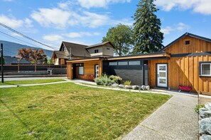 A modern two-story house with a garage, a well-maintained lawn, and a large tree in the background. - Riverside by Cowichan Lake Cottages (Lake Cowichan)