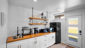 Una cocina moderna con armarios blancos, una encimera de madera y un refrigerador negro. Hay dos estantes sobre la encimera con adornos y utensilios de cocina.
