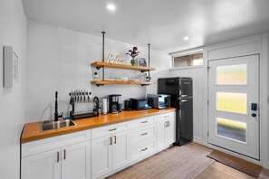 A modern kitchen with white cabinets, a wooden countertop, and a black refrigerator. There are two shelves above the counter holding decorative items and kitchenware. - Riverside by Cowichan Lake Cottages (Lake Cowichan)