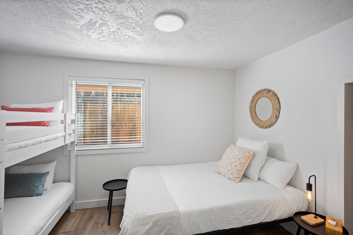 A bedroom with a bunk bed, a single bed, a small table, and a wall-mounted light fixture.