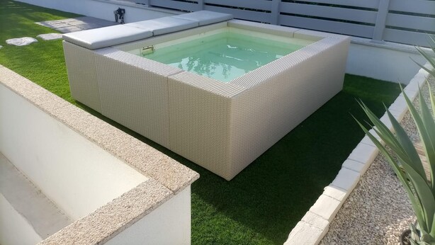 A rectangular outdoor hot tub with a white wicker surround, set on a well-maintained lawn with a white fence in the background. - Villa 21 - Four Bedroom Villa, Sleeps 8 (Budoni)